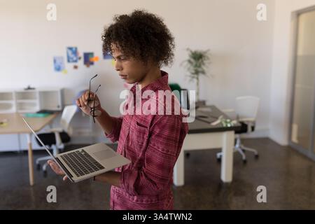 Young man holding laptop and glasses, concentrating in modern office workspace, copy space Stock Photo