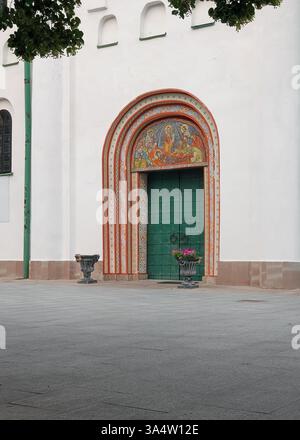 Church entrance gate with green wooden door. Old church with painted wooden door and mosaics above it. Stock Photo
