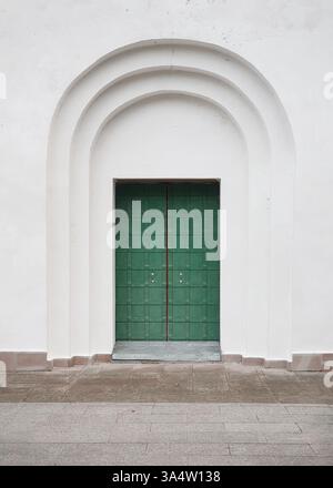 Old green door in white wall of a church. Old painted wooden door with forged metal elements. Stock Photo