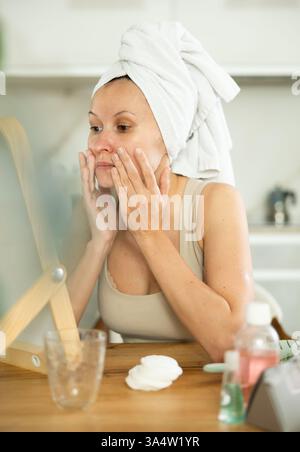 Middle-aged woman examining her facial skin looking in the mirror put on the table Stock Photo