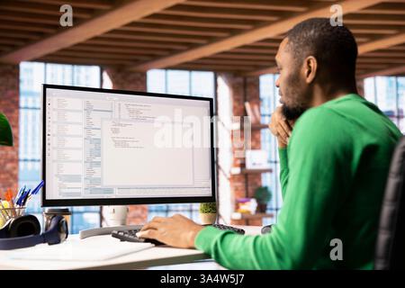 Programmer types code into PC, entering commands, running script. African american IT specialist in apartment office fixing errors in application, implementing new features Stock Photo