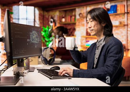 Senior programmer in artificial intelligence focused startup drinking coffee, coding and debugging applications. Experienced IT professional doing code testing and quality assurance, enjoying beverage Stock Photo