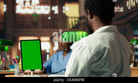 Young man medical student does research for exams next to chroma key, reviewing pharmacology papers under a green lamp. Focusing on exam preparations and their career in medicine. Camera B. Stock Photo