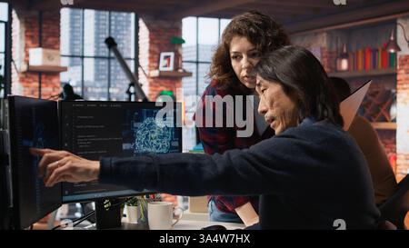 IT engineers cooperating in AI focused startup, debugging applications, crosschecking between PC and laptop. Coworkers doing code testing and quality assurance on devices, camera A Stock Photo
