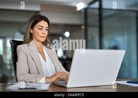 Busy middle aged business woman working in office looking at laptop. Stock Photo