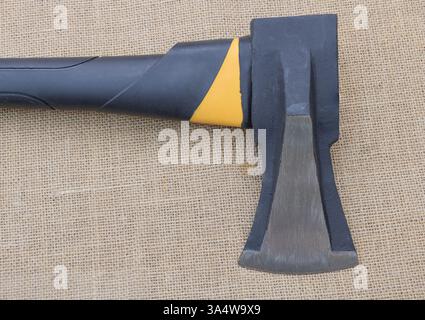 A straight black and yellow ax with an oversized head, resting on burlap fabric. Stock Photo