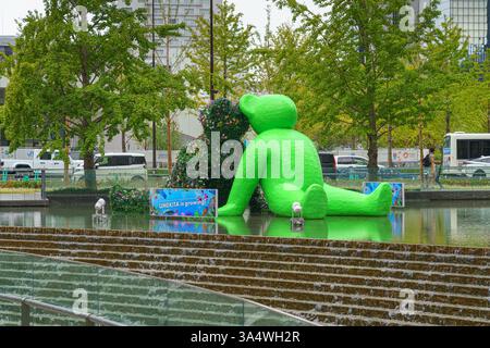 Osaka, Japan - Sep 22 2024, panoramic view of two sculptures of teddy bears sitting by the water in Umekita Plaza, one green and second from foliage o Stock Photo