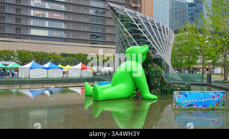 Osaka, Japan - Sep 22 2024, panoramic view of two sculptures of teddy bears sitting by the water in Umekita Plaza, one green and second from foliage o Stock Photo