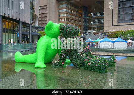 Osaka, Japan - Sep 22 2024, panoramic view of two sculptures of teddy bears sitting by the water in Umekita Plaza, one green and second from foliage o Stock Photo