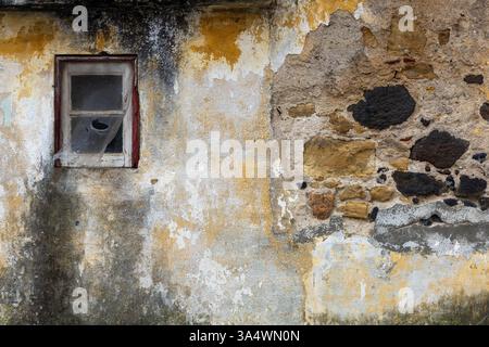 Ancient building closeup​​ of rough​ surface brick​ wall​ concrete plaster​ for​ vintage​ background. Rough ocher cement colors and green moss. Stock Photo