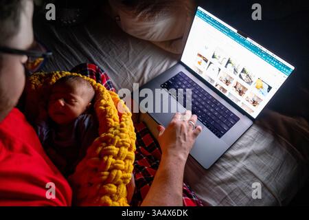 Father Holding Baby While Using Laptop in Dim Light Stock Photo