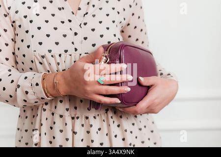 Woman in heart-patterned dress holds a purple clutch, showcasing jewelry. The image highlights fashion details such as a blue heart ring and delicate Stock Photo