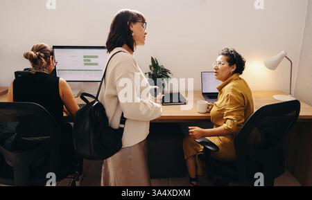 Colleagues collaborating and working in an office environment with laptops and reports visible on desks. Stock Photo