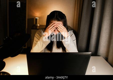 Woman working on computer late evening at home office. Concentrated female freelancer trying to solve business problems. Working and suffering from we Stock Photo