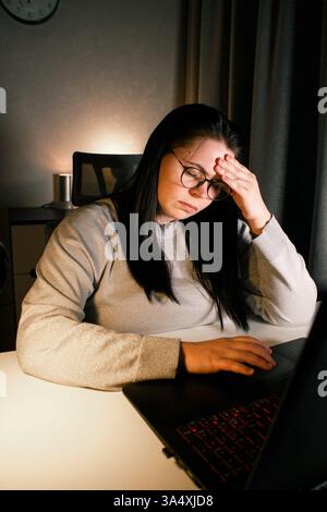 Hard working woman works on computer in her home office and tries to solve work problems. Feeling despair and burnt out from job issues Stock Photo