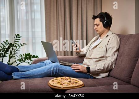 freelancer man using smart phone and laptop on sofa at home Stock Photo