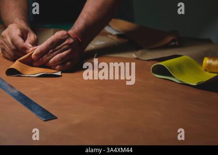 Shoemaker stitching leather pieces on wooden table in workshop Stock Photo