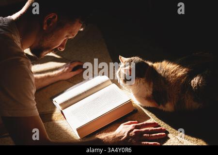 Guy Reading a Book Next to a Cat. Home Environment, Love and Friendship Between a Human and a Pet Stock Photo