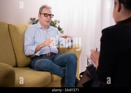 Senior man talking with a female therapist during a counseling session, expressing emotions and receiving professional support in a comfortable settin Stock Photo