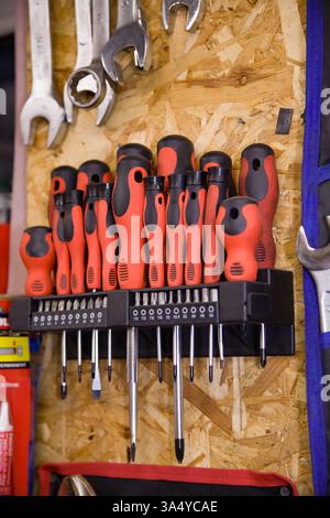 A set of various screwdrivers with red rubber handles is hanging on a special mount on the wall. Stock Photo