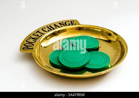 Brass Pocket Change tray with black lettering and a circular pile of poker chips on a white background. Stock Photo
