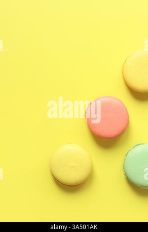 Bright French macarons on yellow background, top view. Assortment of multi-colored macarons with different flavors. Delicious pastries, flat lay. Food Stock Photo
