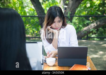 Two young business women sitting at table using laptop and smartphone in coffee shop cafe. Blogging Freelancers working. Woman using smartphone, busin Stock Photo