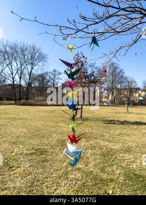 Origami paper cranes in bright colors flying in the wind on a tree vertical Stock Photo