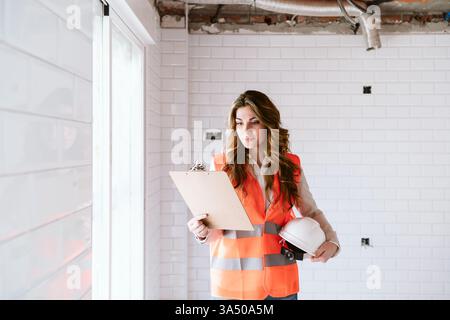 Professional female architect inspecting a kitchen at a construction site. She reviews blueprints on a laptop, emphasizing kitchen renovations and real estate development. Ideal for construction, architecture, and on-site project management visuals. Stock Photo