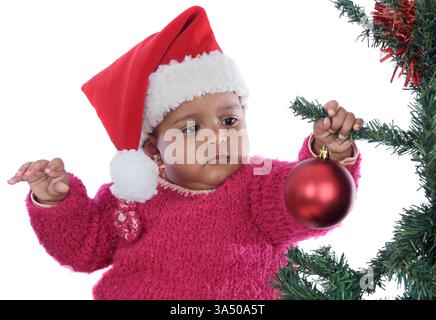 Adorable baby girl plays near a Christmas tree in a white studio setting. The festive scene conveys holiday mood and seasonal charm. Perfect for Christmas campaigns, family content, and seasonal promotions. Stock Photo