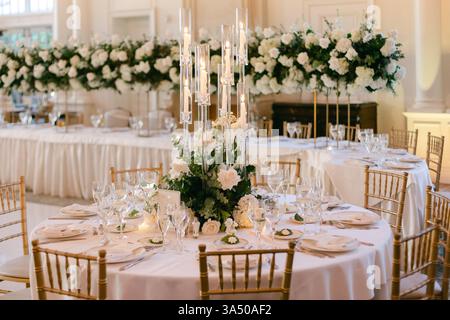 A stunning wedding reception table with white flowers, crystal glassware, and golden chairs in a bright setting. Stock Photo