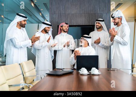 Group of corporate Arab businessmen in kandoras attending a meeting in a Dubai office. A diverse team engages in brainstorming with a focus on partnership and planning. Ideal for topics on Middle East business, Emirati professionals, and corporate meetings. Stock Photo