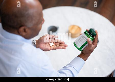 Middle-aged Black man examining the ingredients on a medicine bottle while seated on a sofa at home. The image highlights medication awareness and safe dosing in a domestic setting. Suitable for healthcare, patient education, and lifestyle topics related to supplements and medicines. Stock Photo