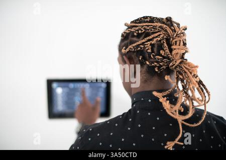 African man interacting with a smart home screen control system in a modern house. A strong fit for home automation, connected devices, and energy management content. Great for tech lifestyle and smart living campaigns. Stock Photo