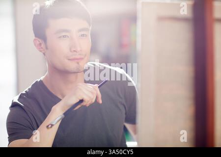 Chinese artist at work in his studio, painting on an easel with brushes and oil paints nearby. A focused, creative environment that showcases concentration, inspiration, and studio-based artistry. Stock Photo