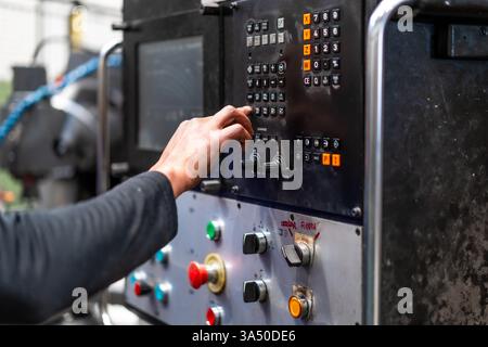 Faceless mixed-race male worker operates a control panel in an industrial factory. This close-up scene highlights manufacturing, machinery and workplace technology on the factory floor. Stock Photo