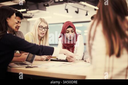 A focused diverse group of business people sits around a table brainstorming and discussing plans in a modern office. This teamwork scene highlights startup culture and inclusive leadership. Perfect for corporate communications, meetings, and strategy imagery. Stock Photo