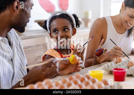 Family painting Easter eggs together at table, sharing joyful creative moments Stock Photo