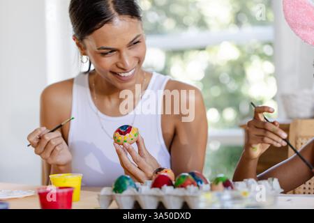 Smiling woman painting colorful easter eggs with child at home during holiday Stock Photo