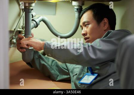 Plumber cleaning a clogged pipe under a kitchen sink. A focused maintenance shot that conveys repair work, tools, and home improvement. Stock Photo