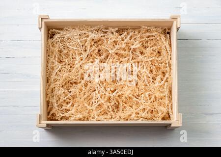 Empty wooden gift box with natural shredded crinkle-cut paper filler on light blue wooden background Stock Photo