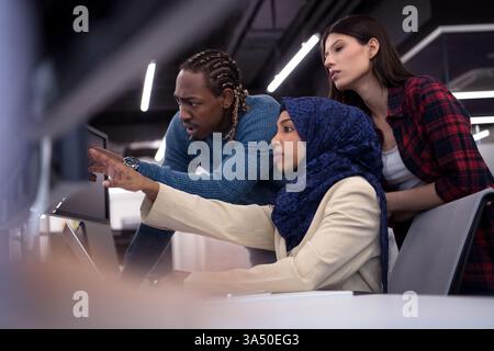 Young multiethnic software developers collaborate in a modern startup office, working together on laptops. This professional scene emphasizes teamwork, technology, and innovation. Stock Photo