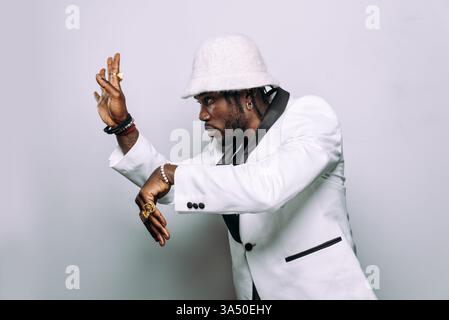 African American male wearing a hat and jewelry looking away against a white studio background. This dynamic dancer image conveys attitude and movement, suitable for fashion and entertainment campaigns. Copy space on the clean background makes it versatile for posters, ads, and social content. Stock Photo