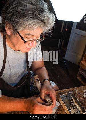 Luthier Carlos Roberts works at his workshop in Cremona, Italy, crafting violins. This detailed studio scene highlights traditional craftsmanship and handmade instruments. Stock Photo