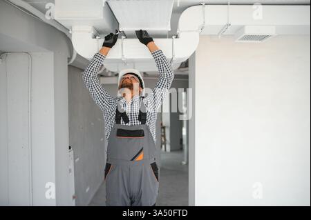 Indian male worker installing ducted pipe system for ventilation and air conditioning in an apartment building Stock Photo