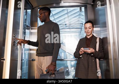 Black businessman wearing eyeglasses standing with caucasian female colleague and pressing button in elevator at the office Stock Photo