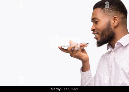 African American man uses a voice assistant on a smartphone, depicted against a white background with clear copy space. This tech focused portrait is ideal for mobile apps, AI, or digital services campaigns. Clean close-up style supports bold type and headline integrations. Stock Photo