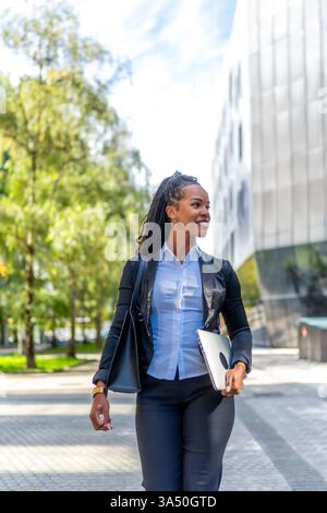 Vertical image of a stylish Latina businesswoman walking through the city. This bold urban portrait conveys confidence, ambition, and professional presence. Ideal for corporate branding, startups, and city life campaigns. Stock Photo
