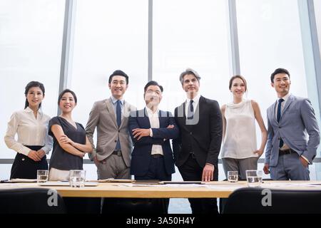 Confident Chinese business professionals gathered around a conference table in a meeting room. They project teamwork and focus, ready to discuss strategy. Ideal for corporate communications, diversity, and global business themes. Stock Photo