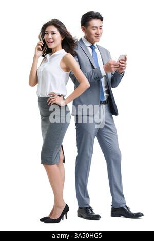 Chinese businessman and business woman using smartphones standing against white background in studio Stock Photo